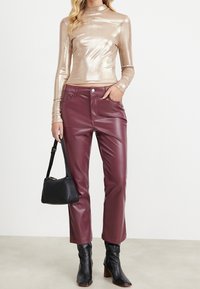 Metallisk guld långärmad topp, vinröda läderbyxor med hög midja, svart handväska och svarta klackstövlar. Slät textur och tight passform.