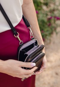 Black leather crossbody bag with silver hardware, zip compartments, and a zigzag patterned interior. Constructed with a flat design.