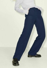 Marinblå byxor med vida ben och slät textur, med fickor framtill och diskreta veck vid midjan. Bärs med svarta snörskor.