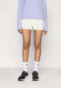 Lys lilla langermet topp, kremfargede shorts, svarte joggesko og hvite sokker med svart logo. Har flate sømmer og avslappet passform.