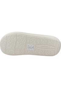 Suela de un zapato hecha de goma, con una superficie texturizada y con un patrón de formas ovaladas. Incluye etiqueta del fabricante. El color es blanco roto.