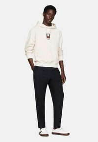 Sudadera blanca con logo, pantalones negros ajustados y zapatillas blancas con detalles en marrón. Tejido suave y corte relajado en general.