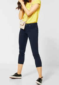 Marina korta byxor med smal passform, kombinerade med en gulrandig t-shirt och svarta sneakers. Rosa axelväska med en klaffdetalj.