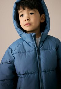 Blauwe gewatteerde jas met capuchon, voorzien van een rits aan de voorkant en een geborduurd patroon. Glad materiaal en een ontspannen pasvorm, geschikt voor koelere weersomstandigheden.