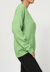 Pull en laine vert, coupe ample, col rond, manches longues, texture douce, poignets côtelés, associé à un pantalon noir.