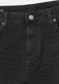 Nærbillede af sorte denimjeans, som viser knap med præget logo, bæltestropper, syninger og nitter på forlommerne. Størrelsesmærke synligt indeni taljen.