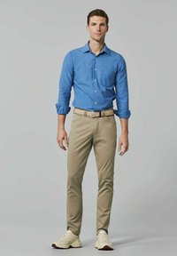 Lichtblauw overhemdd met opgerolde mouwen, in combinatie met beige broeken en witte sneakers. Het overhemd heeft een voorzak en een kraagontwerp.