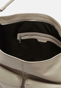 Sac à main en cuir beige avec une texture lisse. Présente une poche zippée et un intérieur doublé, mettant en avant des lignes épurées et un minimum de quincaillerie.