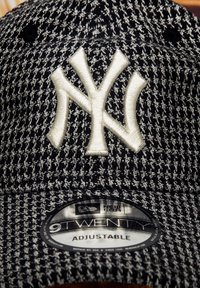 Casquette de baseball à motif pied-de-poule noir et blanc avec un logo NY brodé en relief et une sangle ajustable. Étiquette New Era 9Twenty visible.