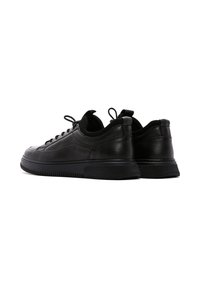 Black leather sneakers with a textured finish, rounded toe, flat laces, and a thick rubber sole. Minimalist design with a smooth profile.