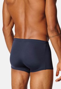 Mörkblå simshorts med en figurnära design; slät yta; mellanhög midja och inga synliga sömmar. Har en kant för bakfickan.