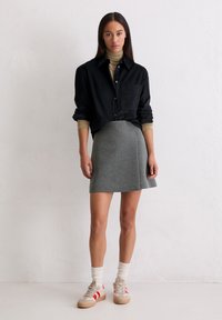 Chemise noire boutonnée, jupe grise ajustée, baskets beiges avec accents rouges, et chaussettes blanches texturées. Design simple et épuré, look polyvalent.