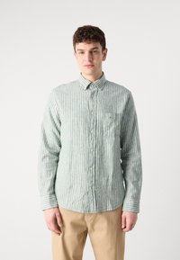 Camicia a righe in lino verde chiaro e bianco, con taschino sul petto e colletto a bottoni; maniche lunghe con dettagli sui polsini.