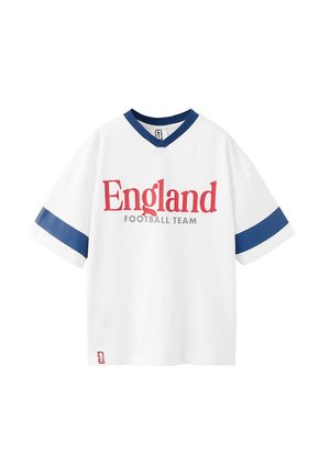 Tricou de fotbal alb cu mâneci scurte, dungi bleumarin pe mâneci și guler, cu text roșu "England" și text gri "Football Team" pe față.