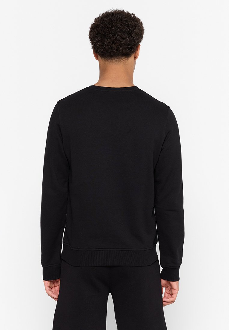 Sudadera negra en mezcla de algodón, con cuello redondo, mangas largas y puños y dobladillo acanalados. Diseño simple sin logotipos ni patrones visibles.
