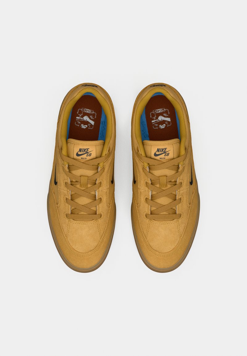 Baskets Nike SB en daim marron clair, avec un swoosh noir, des lacets beiges et des accents intérieurs bleus et marron. Semelle extérieure en caoutchouc incluse.