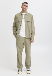 Vaaleanoliivinvihreä paita ja siihen sopivat housut, jotka on valmistettu teksturoidusta kankaasta. Paidassa on napillinen etuosan taskuilla varustettu malli. Valkoinen graafinen T-paita alla.