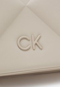Clutch in pelle color crema con un design a losanghe trapuntato e logo "CK" impresso in una tonalità sobria e abbinata.