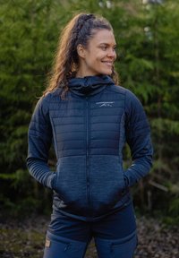Marineblå isoleret jakke med en struktureret hætte, lynlås foran og to sidelommer. Har en quilted øverste sektion og glat nederste stof.