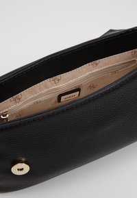 Sort struktureret lædertaske med en guld trykknaplukning. Indersiden har en beige foering med en lynlås lomme og "Guess" logoet.
