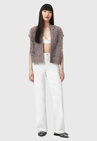 Cardigan grigio chiaro con texture, corpo peloso, maniche corte e orlo a costine, abbinato a pantaloni bianchi a vita alta e scarpe scure.