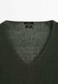 Ciemnozielony sweter z lnu o luźnym splotcie i dekolcie w kształcie litery V, z subtelnym wzorem siateczkowym w pobliżu kołnierza i metki.
