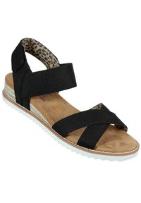 Zwarte stoffen sandaal met kruislings leren banden, faux-suède voetbed en witte rubberen zool. Interieur heeft een luipaardprintdetail.