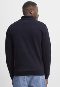 Marineblaues Sweatshirt mit hohem Kragen, gerippten Bündchen und Saum, weicher Textur und einem einfachen, klaren Design. Getragen über hellblauen Jeans.