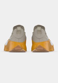 Baskets avec une tige en tissu gris et une semelle en caoutchouc jaune. Dotées de languettes à l'arrière et d'un logo blanc sur le côté. Forme arrondie.