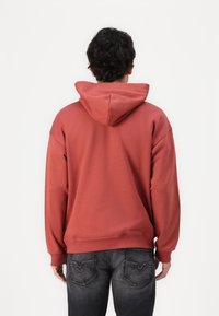 Red hoodie with a relaxed fit, featuring a drawstring hood and ribbed cuffs. The fabric appears soft with a smooth texture.