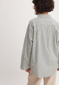 Striped shirt made of soft fabric featuring blue and white vertical lines, a collar, and buttoned cuffs, with a relaxed fit and curved hem.