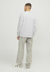 Grå sweatshirt med lange ærmer, ribbede kanter og søm. Parret med lyse, falmede, vide jeans og hvide sneakers med sorte striber.