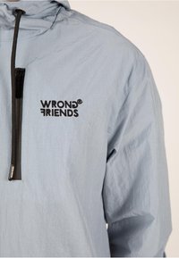 Helltürkise Nylon-Hoody mit einem Viertelreißverschluss und gesticktem "WRONG FRIENDS"-Logo in Schwarz. Verfügt über eine strukturierte Oberfläche und eine verstellbare Kapuze.