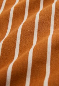 Tissu en coton de couleur orange chaud avec de fines rayures blanches. La texture semble douce et légèrement duveteuse, mettant en valeur des variations subtiles de couleur.