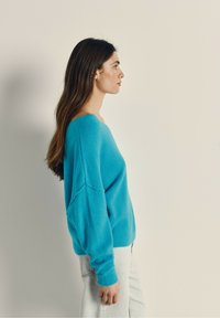 Lyseblå oversized sweater med en bred halsudskæring, lange ærmer og blød tekstur, parret med lyse jeans.