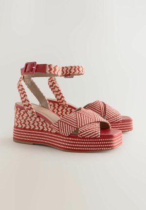 Red and cream woven espadrille platform sandals with cross strap design, buckle closure, and decorative textured patterns on the wedge.