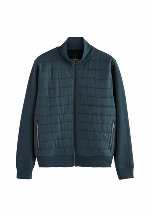 Chaqueta de un tono verde azulado oscuro con cremallera frontal, que presenta paneles superiores acolchados y secciones inferiores sólidas. Cuello y puños de canalé. Bolsillos laterales con cremallera.