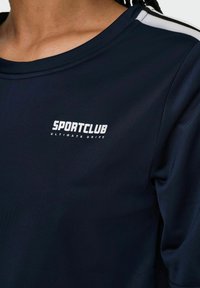 Navy Sportshirt aus atmungsaktivem Material, mit Rundhalsausschnitt, kurzen Ärmeln und weißen Akzenten an den Schultern sowie dem "SPORTCLUB"-Logo.