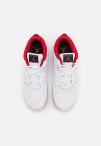 Scarpe da ginnastica bianche con accenti rossi, dotate di texture perforata, chiusura con lacci e un'etichetta nera con logo sulla linguetta.