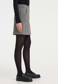 Minifalda de espiga en blanco y negro con cintura ajustada, bolsillos laterales, llevada con medias opacas negras y mocasines negros. Textura suave.
