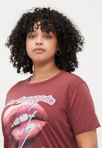 Maroon T-shirt made of soft cotton featuring a graphic design of lips and a lightning bolt with glitter accents. Relaxed fit and short sleeves.