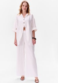 Witte cropped button-up shirt met korte mouwen, gecombineerd met wijde witte broeken. Glad textuur en ontspannen pasvorm. Minimalistisch ontwerp.