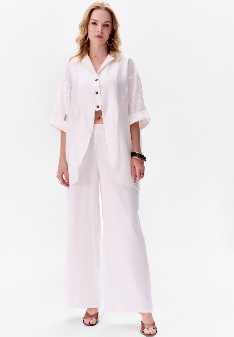 Witte cropped button-up shirt met korte mouwen, gecombineerd met wijde witte broeken. Glad textuur en ontspannen pasvorm. Minimalistisch ontwerp.