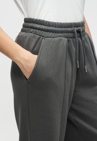 Γκρι φόρμα με κορδόνι στη μέση, διαθέτει πλαϊνές τσέπες και ελαστική ζώνη μέσης. Το ύφασμα είναι απαλό και λεία υφή.