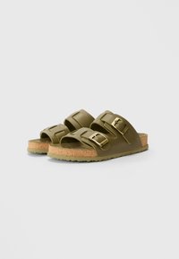Grønne sandaler med to brede remme, gyldne spænder og en kork-mellemsål. Tekstureret gummisål for godt greb. Minimalistisk design og åben tå stil.
