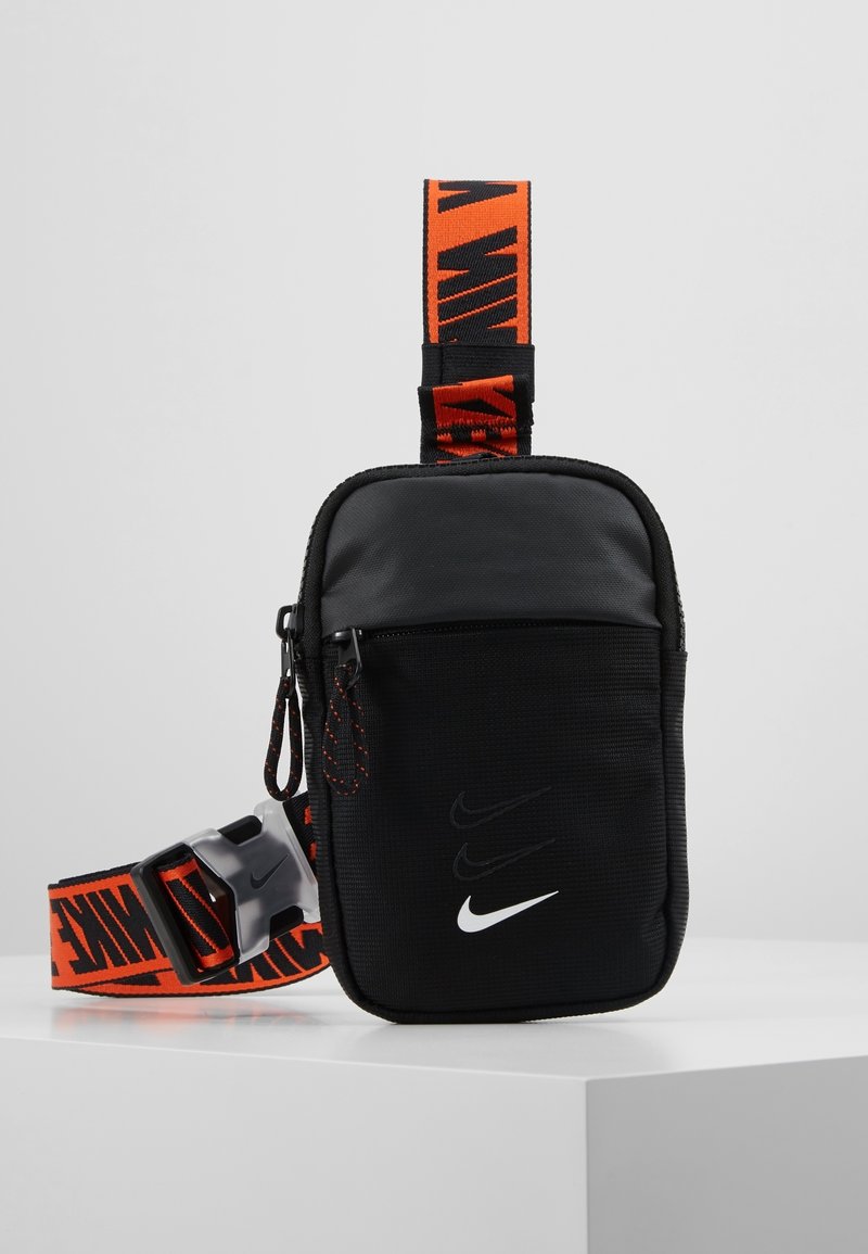 Černý a tmavě šedý pouzdro Nike se třemi logy swoosh na přední straně a oranžovým popruhem s černým brandingem Nike a sponou.