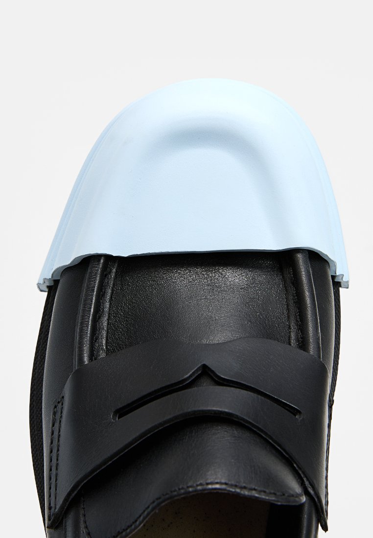 Scarpa in pelle nera con punta in gomma blu, caratterizzata da una forma curva, superficie texturizzata e una striscia decorativa sulla parte superiore.