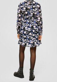 Svart klänning med blommigt mönster i blått och vitt, långa ärmar, åtsittande midja, plisserad kjol och nyckelhålsdetalj i ryggen, kombinerad med svarta stövlar.