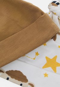 Gorro de algodão castanho com textura canelada, combinado com uma manta branca com estrelas amarelas e um gráfico de ovelha.