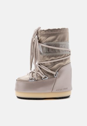 Bota alta beige de invierno con suela gruesa y cordones envueltos, con parte superior acolchada y el nombre de la marca Moon Boot grabado en el lateral.
